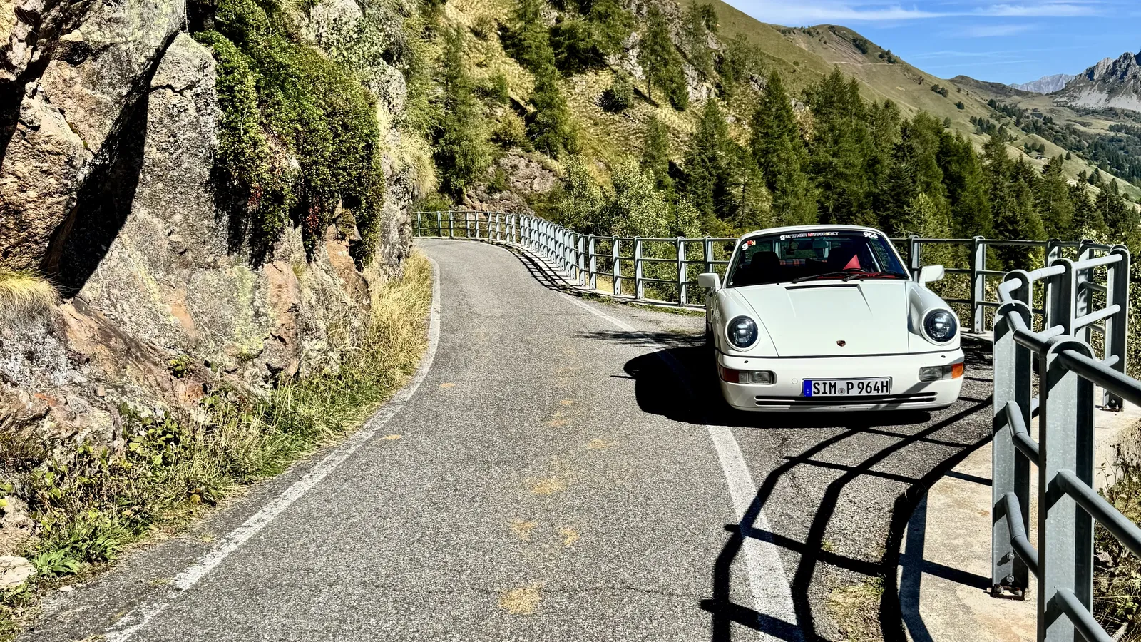 Weißer Porsche 911 auf einer schmalen Bergstraße mit Felswand und Geländer