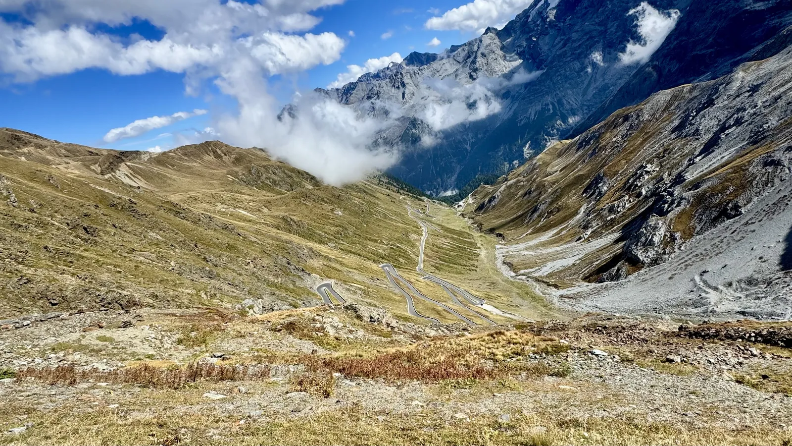 Serpentinen einer Alpenpassstraße zwischen grünen Hängen und schroffen Felsgipfeln