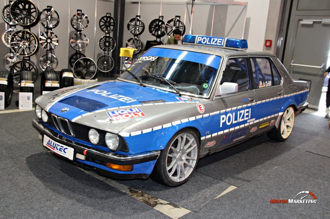 Blauer BMW-Polizeiwagen der 1980er Jahre mit Dachleuchte und Schriftzug auf Oldtimerschau, Felgen hängend an der Wand dahinter