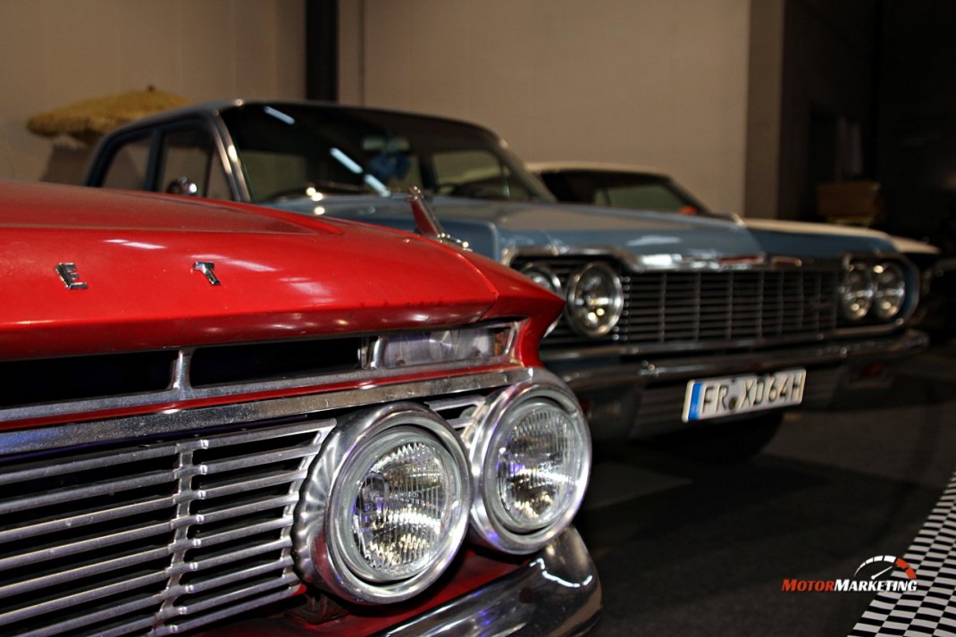 Rote und dunkelgraue Oldtimer-Limousinen mit Doppelscheinwerfern nebeneinander auf Ausstellungsfläche der Automobil Freiburg