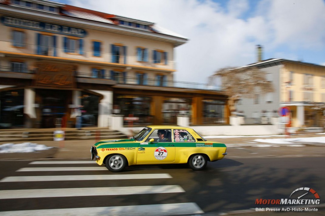 Gelb-grüner Oldtimer-Sedan bei der AvD-Histo-Monte überquert einen Zebrastreifen vor historischen Gebäuden