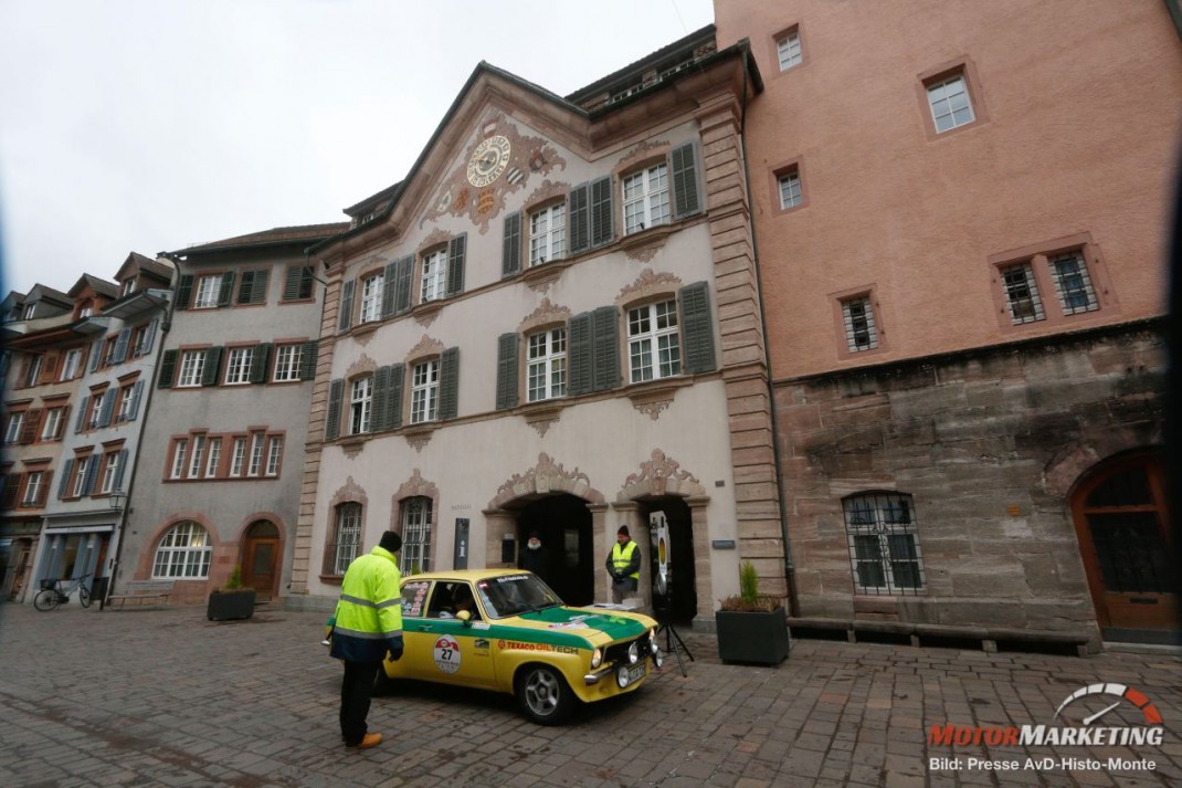 Gelb-grüner Oldtimer-Kleinwagen mit Warnwesten auf Pflasterplatz vor historischem Altstadtgebäude bei der AvD-Histo-Monte