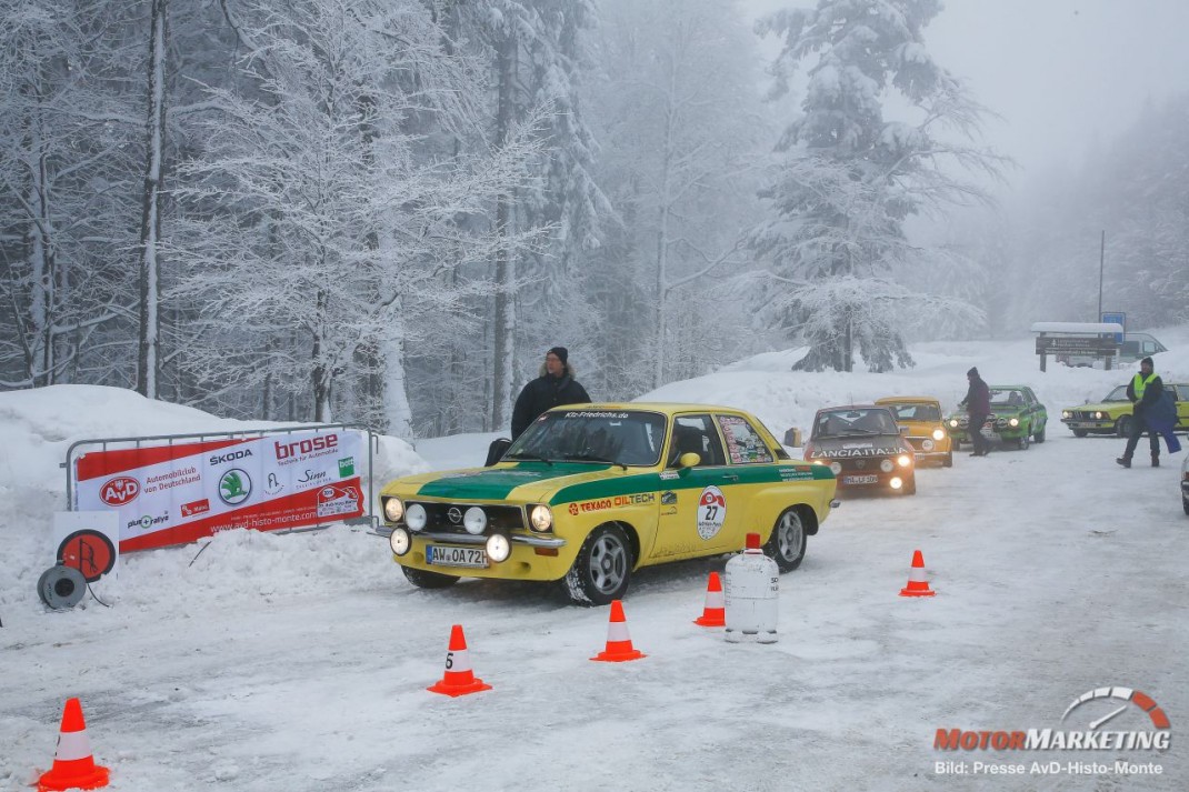 Gelber Youngtimer-Rennwagen beim Slalomtest im Schnee während der AvD-Histo-Monte, dahinter verschneite Waldkulisse und weitere Fahrzeuge