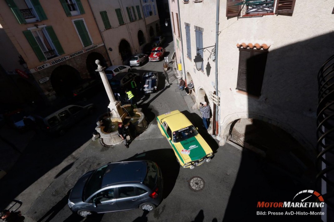 Luftaufnahme einer engen Gasse mit drei Oldtimern bei der AvD-Histo-Monte, ein grün-gelber Wagen manövriert zwischen Fahrzeugen