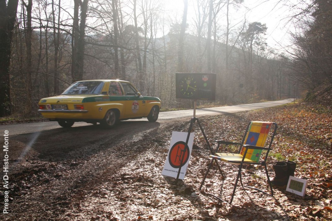 Gelber Opel Ascona nähert sich einer Kontrollstelle der AvD-Histo-Monte Rallye im Wald mit Schildern und Zeitnahme-Equipment
