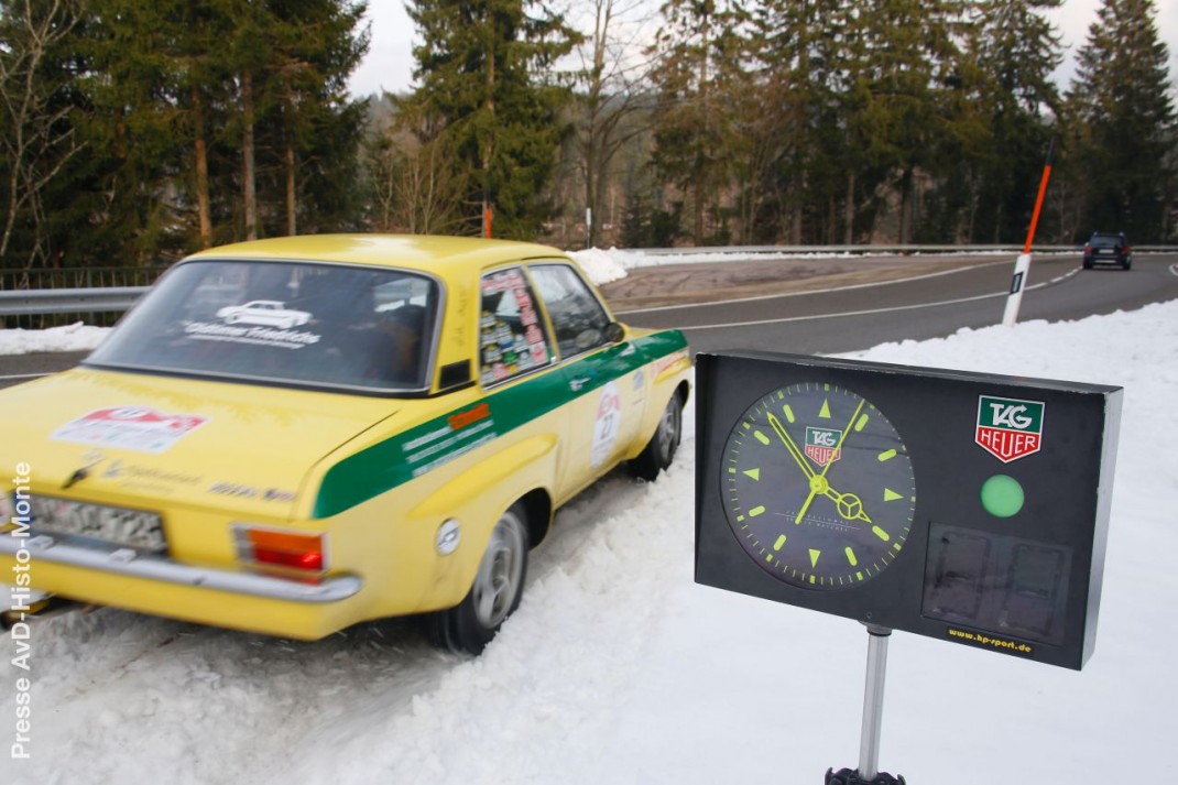 Gelber Oldtimer-Sedan mit grünem Streifen bei der AvD-Histo-Monte, daneben eine Stempeluhr im Schnee