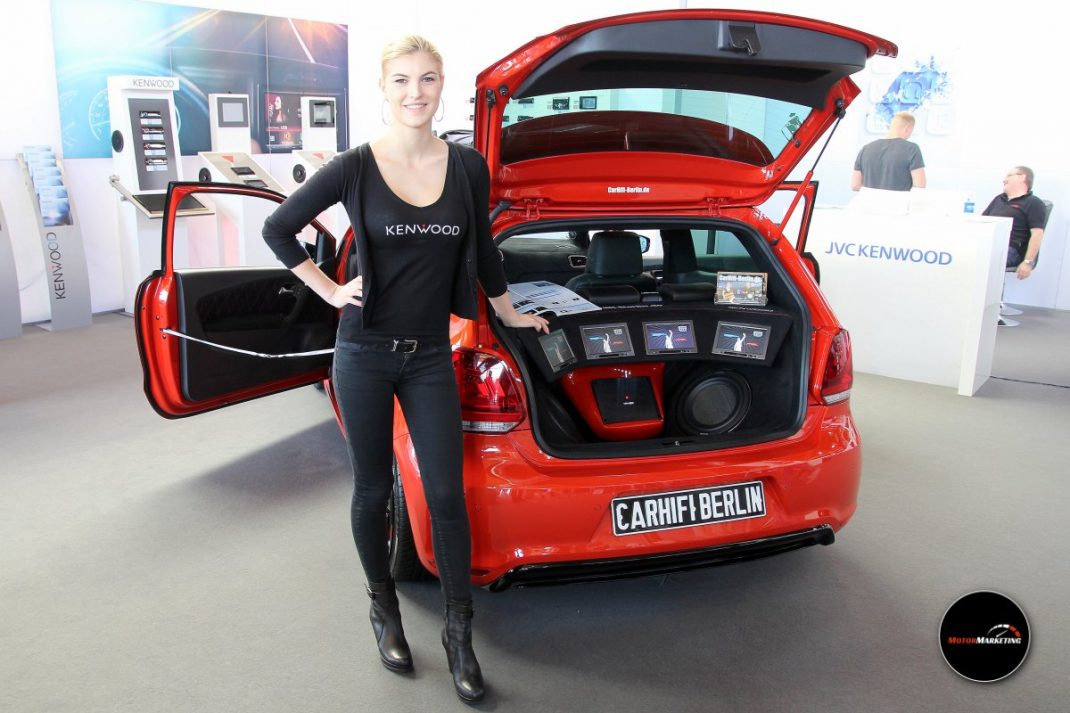 Frau präsentiert roten Tuning-Youngtimer mit offener Motorhaube und Audioanlage auf der TuningWorld Bodensee