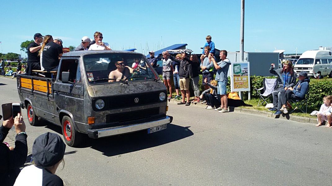 Oldtimer-Transporter fährt mit beladener Ladefläche durch Menschenmenge beim Bulli Festival Fehmarn