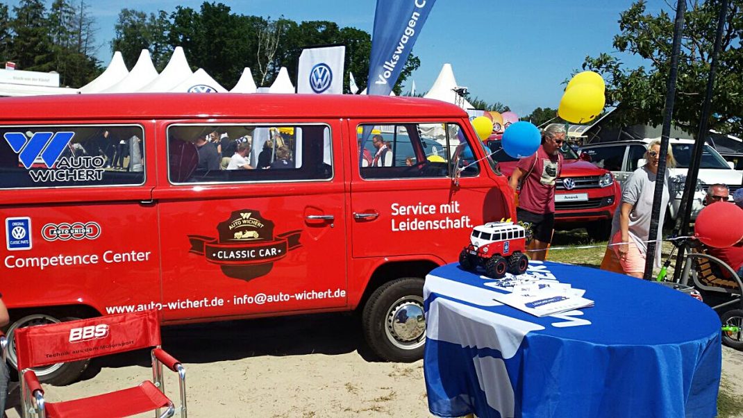 Roter VW-Bulli mit Competence-Center-Branding auf dem Midsummer Bulli Festival, umgeben von weißen Zelten und farbigen Luftballons