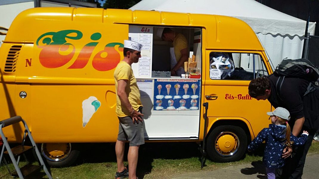 Gelber VW-Transporter mit Eis-Verkaufsstand beim Midsummer Bulli Festival auf Fehmarn, Verkäufer und Besucher an der Serviceluft