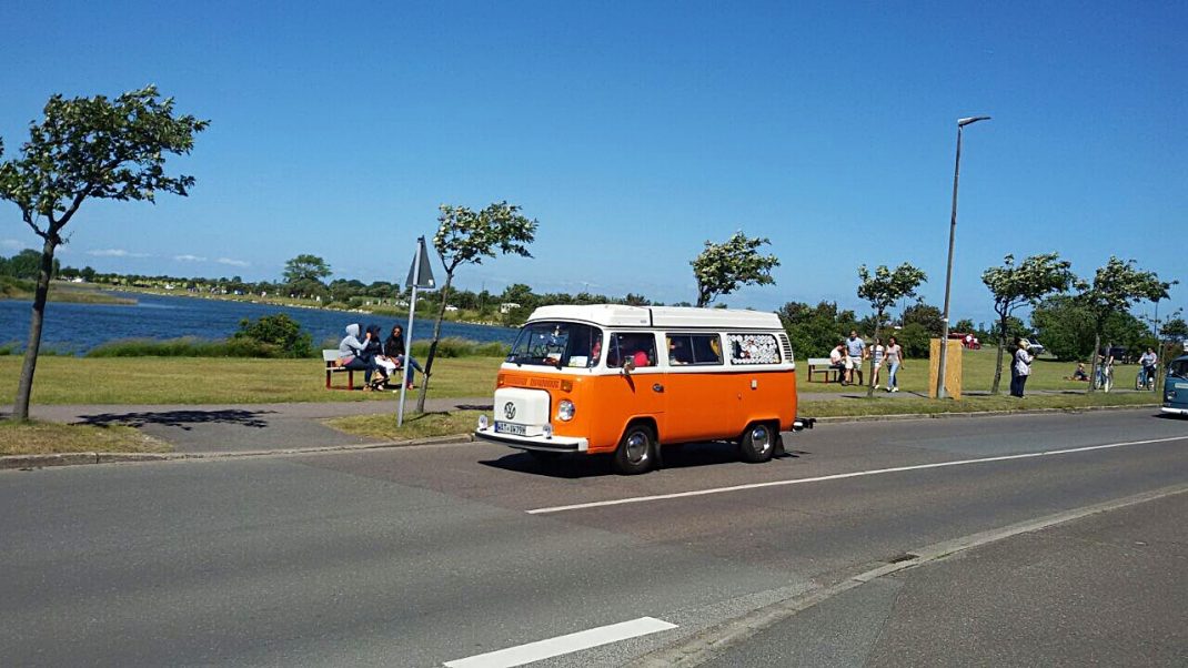 Orangefarbener Oldtimer-Bulli auf Parkplatz am Wasser beim Midsummer Bulli Festival auf Fehmarn