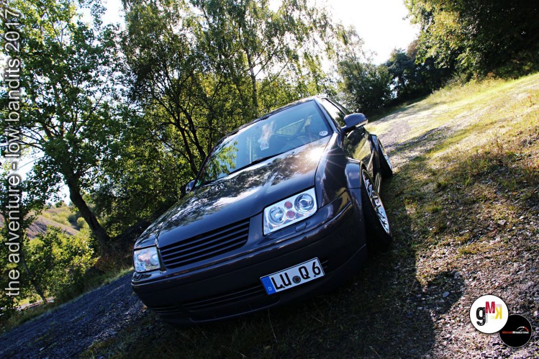 Schwarze Youngtimer-Limousine mit Tuning-Rädern auf Schotterweg zwischen Bäumen während Adventure-Tour