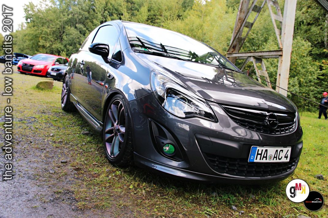 Schwarz-silberner Opel Corsa mit Tuning-Felgen auf Wiese bei Youngtimer-Treffen, weitere Fahrzeuge und Waldkulisse im Hintergrund