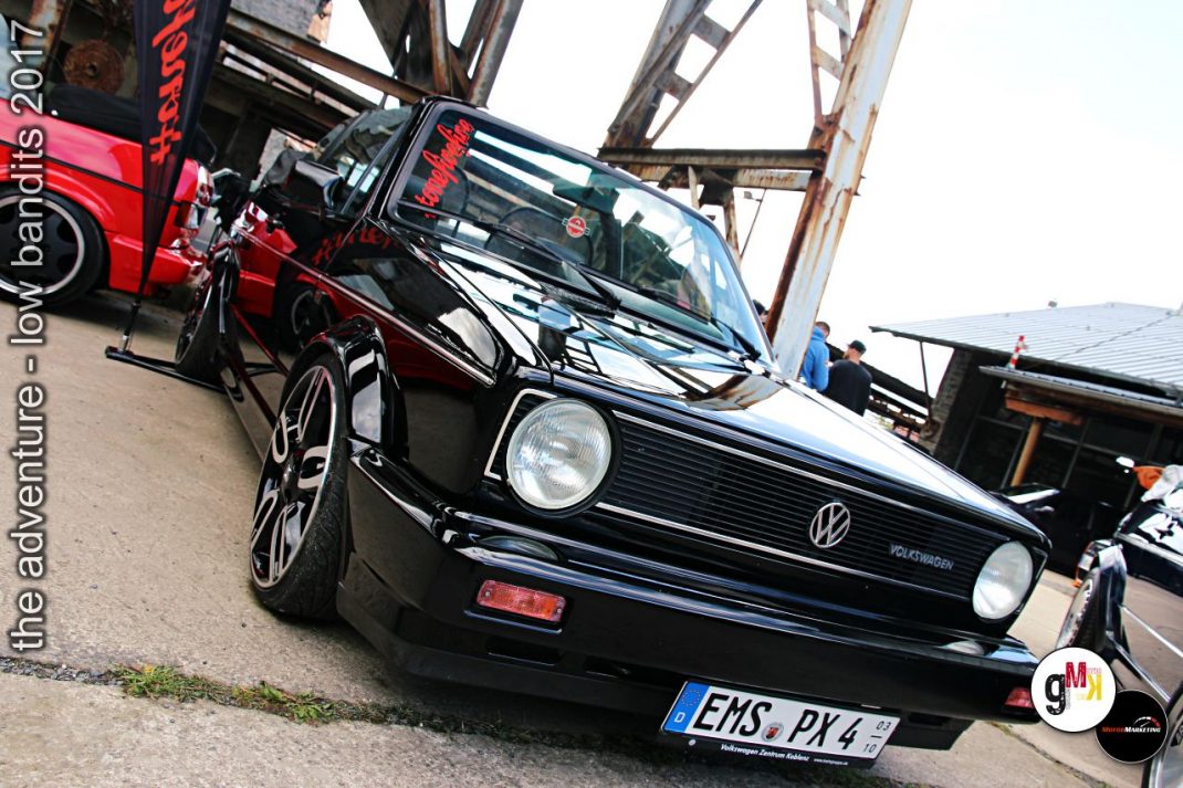 Schwarzer VW Golf Cabriolet mit Dachgestell auf Tuning-Veranstaltung im Steinbruch, daneben roter Oldtimer-Bus