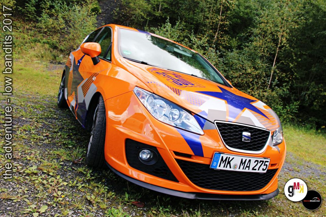 Orangefarbener Youngtimer-Kompaktwagen mit blau-weißem Racer-Design auf Waldweg beim Tuning-Event „The adventure – low bandits 2017