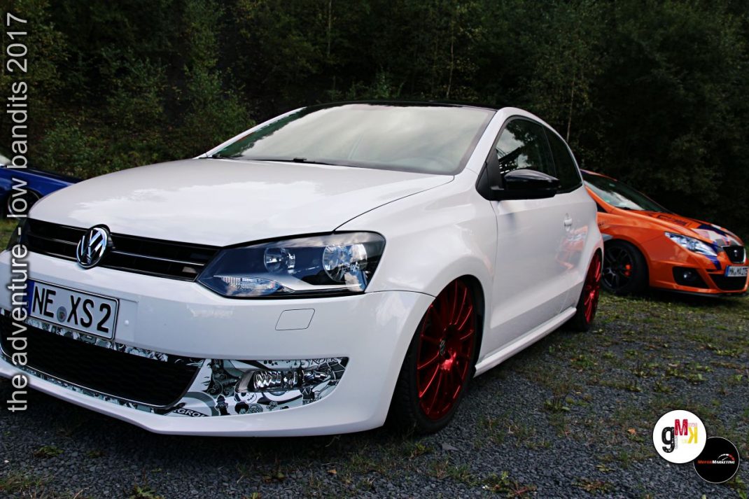 Weißer VW Polo mit roten Felgen und orangefarbenem Youngtimer im Hintergrund beim Tuning-Event „The adventure – low bandits 2017