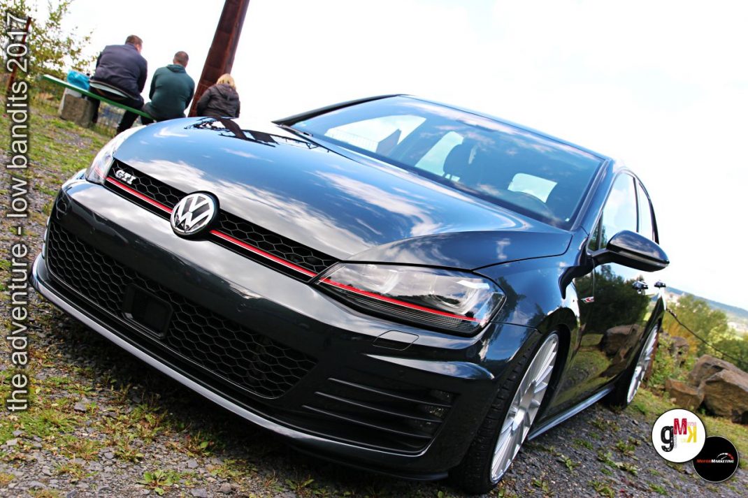 VW Golf GTI Youngtimer auf Kiesplatz bei Tuning-Event mit Besuchern im Hintergrund