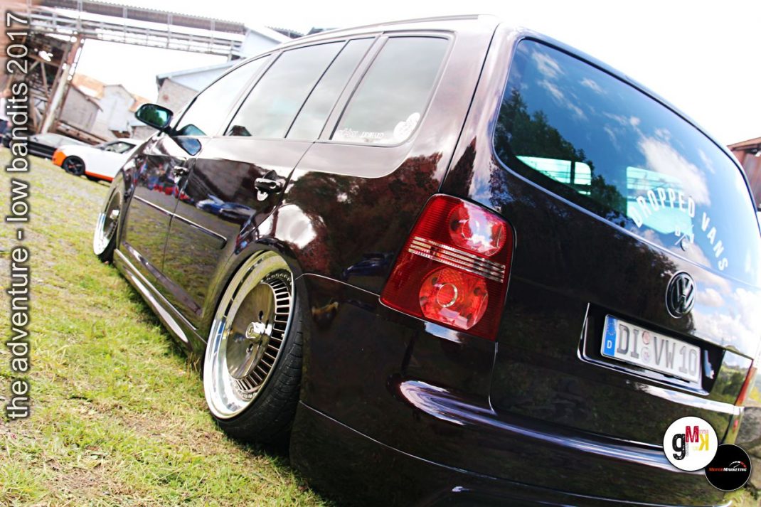 Schwarzer VW-Touran mit Chromfelgen und tiefergelegtem Fahrwerk auf Treffen-Gelände, im Hintergrund weitere Fahrzeuge