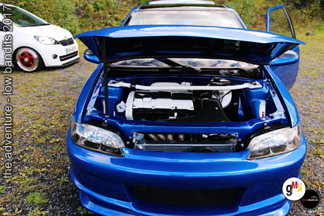 Blauer Youngtimer mit geöffneter Motorhaube zeigt Motorraum, weißer Oldtimer im Hintergrund auf Wiese bei Tuning-Event