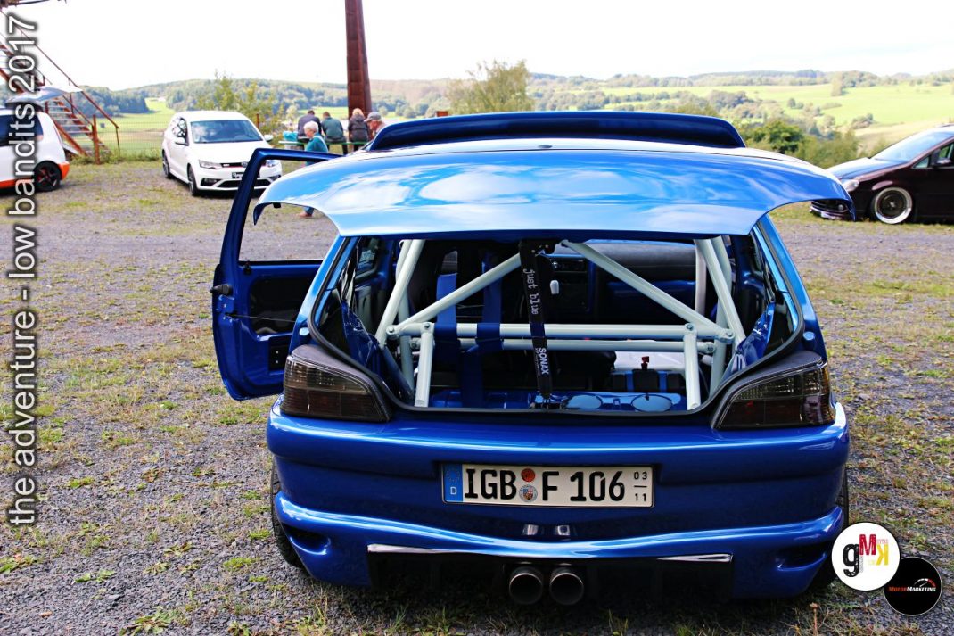 Blauer Youngtimer-Tuner mit offener Heckklappe und Überrollbügel auf Treffen, weitere Fahrzeuge im Hintergrund