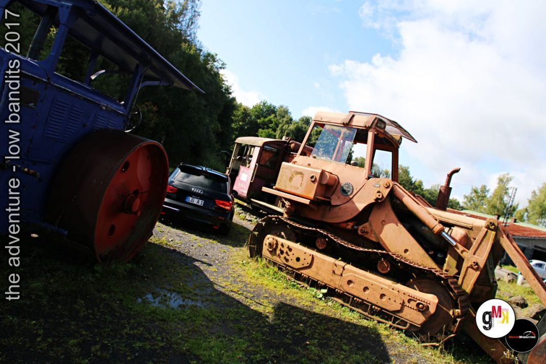 Rostiger Raupenbagger und Oldtimer-Limousine neben blauem Lastwagen auf einem Veranstaltungsgelände