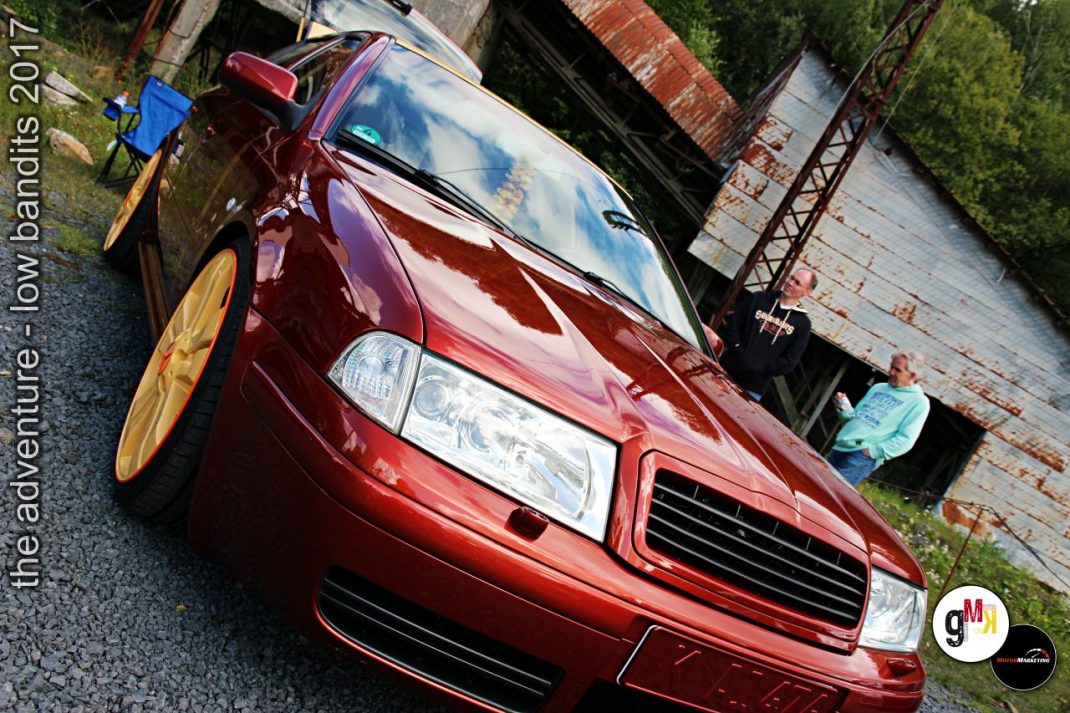 Roter Youngtimer mit Tieferlegung und gelben Felgen an Industriekulisse während Tuning-Event