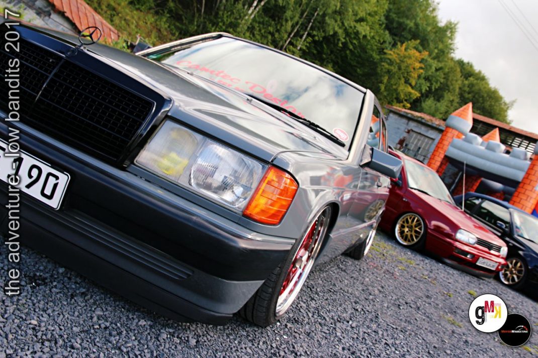 Zwei Youngtimer-Limousinen auf Kiesplatz bei Tuning-Treffen, dunkelblauer Wagen vorn, bordeauxroter Wagen hinten, Wald im Hintergrund