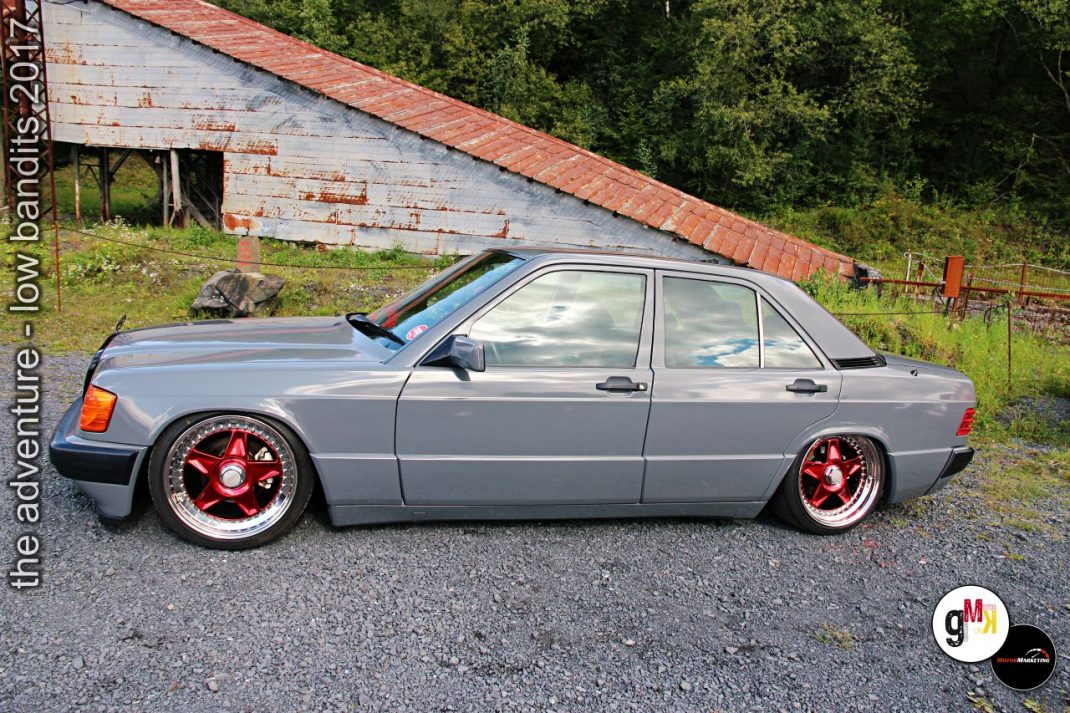 Silbergraue Youngtimer-Limousine mit roten Felgen und tiefergelegtem Fahrwerk vor alter Scheune beim Tuning-Event