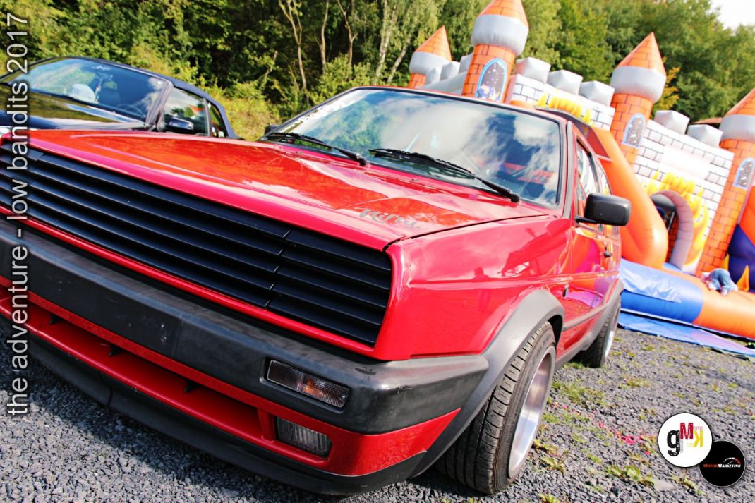 Roter Youngtimer-Sportwagen mit horizontalem Kühlergrill neben aufblasbarem Schloss-Parcours auf Tuning-Event im Grünen