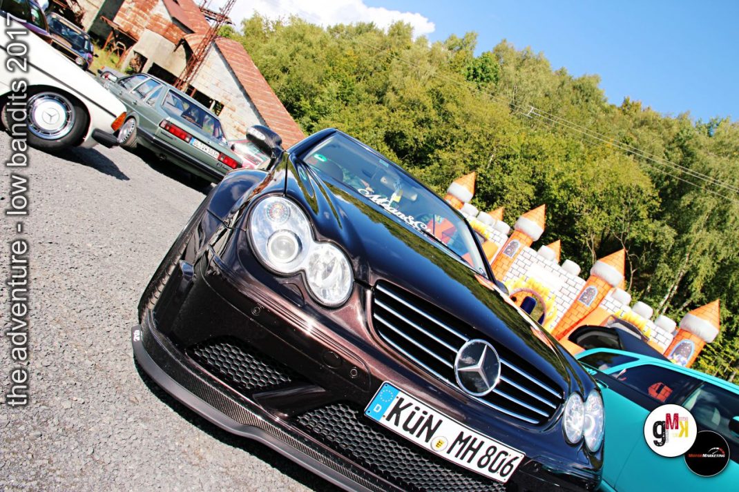 Schwarzer Mercedes-Sportwagen in der Frontansicht auf Veranstaltungsparkplatz mit weiteren Oldtimern und Gebäuden im Hintergrund