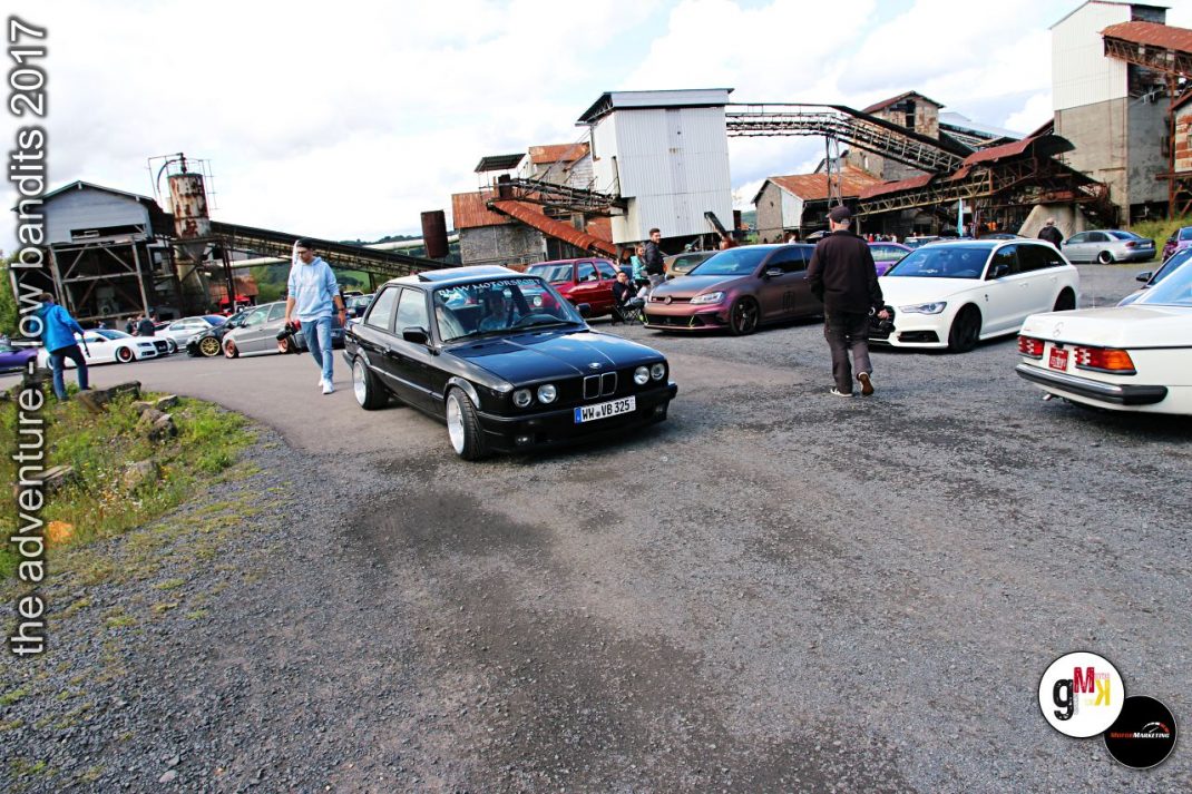 Mehrere Youngtimer-Limousinen und Sportwagen auf einem Gelände mit Industriegebäuden beim Tuning-Treffen Low Bandits 2017