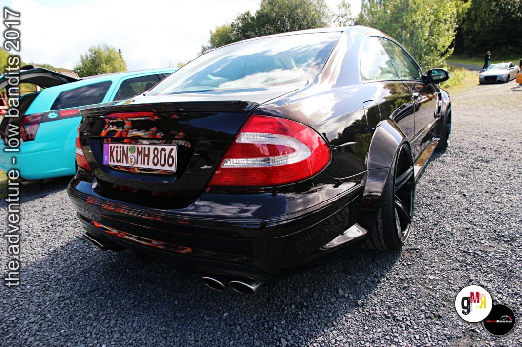 Schwarze Youngtimer-Limousine mit offener Motorhaube auf Parkplatz neben türkisem Oldtimer-Cabrio bei Treffen