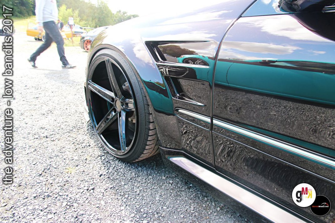 Grün-schwarzer Youngtimer-Limousine mit tiefer Luftfederung und verchromten Rädern bei Tuning-Treffen im Steinbruch