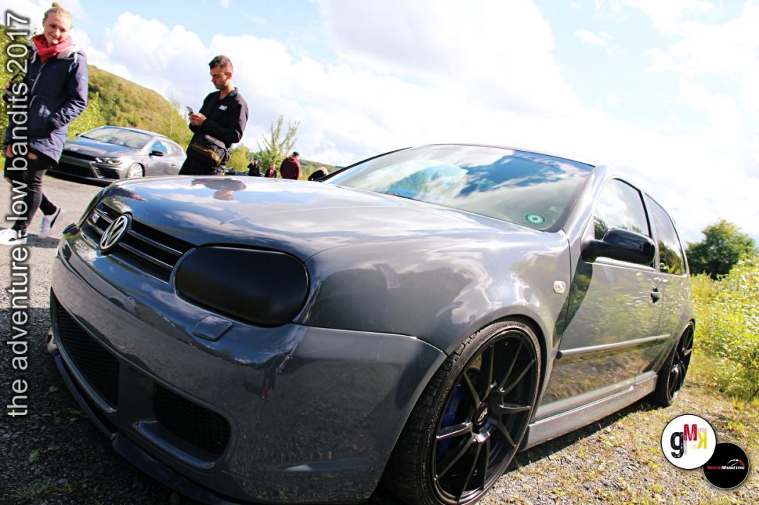 Dunkelblauer Youngtimer-Kompakt mit Tuning-Felgen auf Event-Gelände, Besucher und weiteres Fahrzeug im Hintergrund