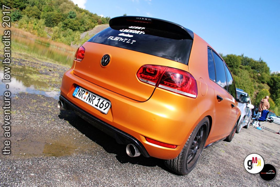 Orange Youngtimer-Kompaktwagen von hinten an Veranstaltungsort mit Steinbruch-Szenerie, Teilnehmer im Hintergrund