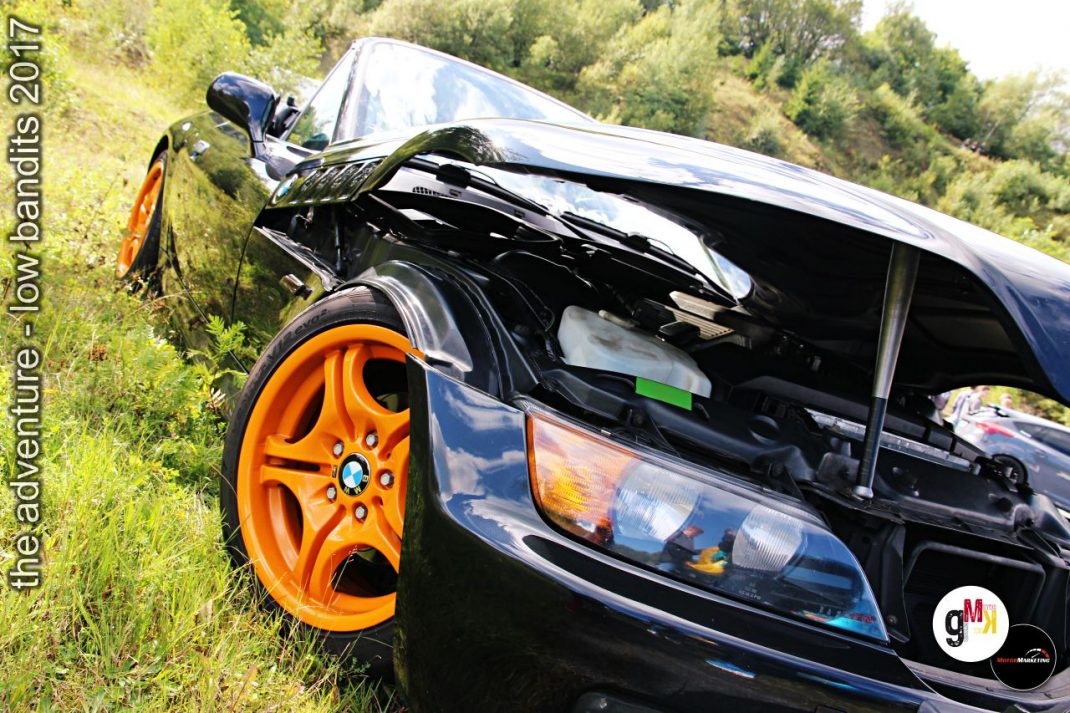 Schwarzer Youngtimer mit orangefarbenen Felgen und tiefer Tuning-Ausführung in grüner Landschaft