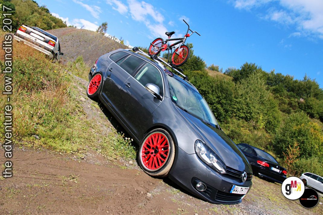 Tiefergelegter Youngtimer mit roten Felgen und Fahrrad auf dem Dach beim Tuning-Event im Steinbruch