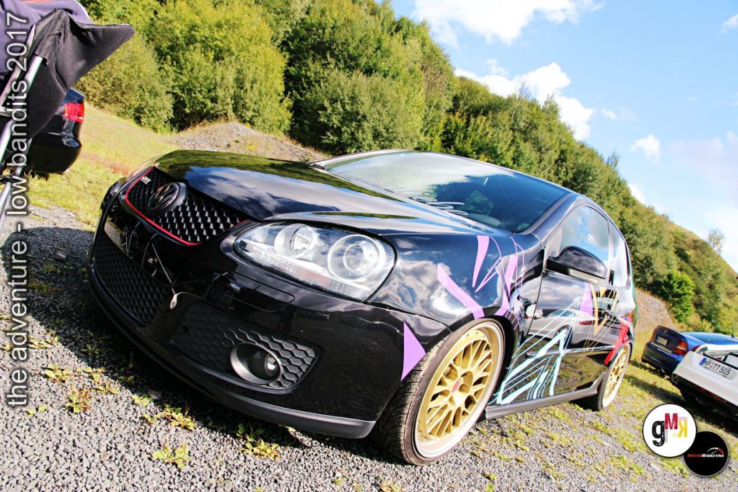 Schwarzer Youngtimer-Kompaktwagen mit goldenen Leichtmetallrädern und Tieferlegung auf Kiesplatz bei Tuning-Event