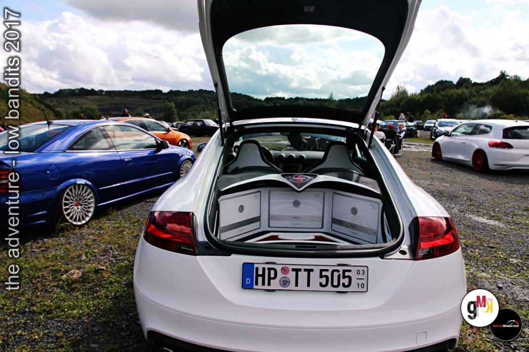 Weißer Sportwagen mit geöffnetem Kofferraum auf Youngtimer-Treffen, dahinter geparkte Fahrzeuge und Wiese
