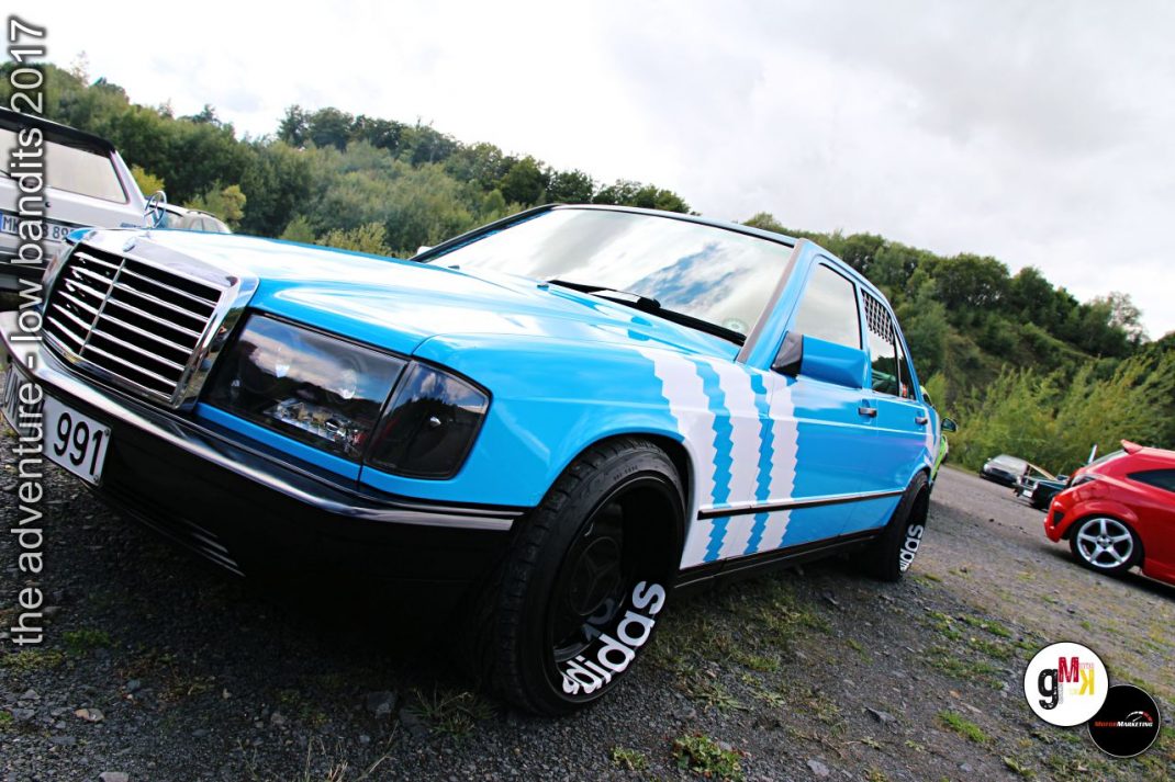 Blau-weißer Youngtimer-Limousine mit Tuning-Streifen in einem Steinbruch neben einem roten Sportwagen