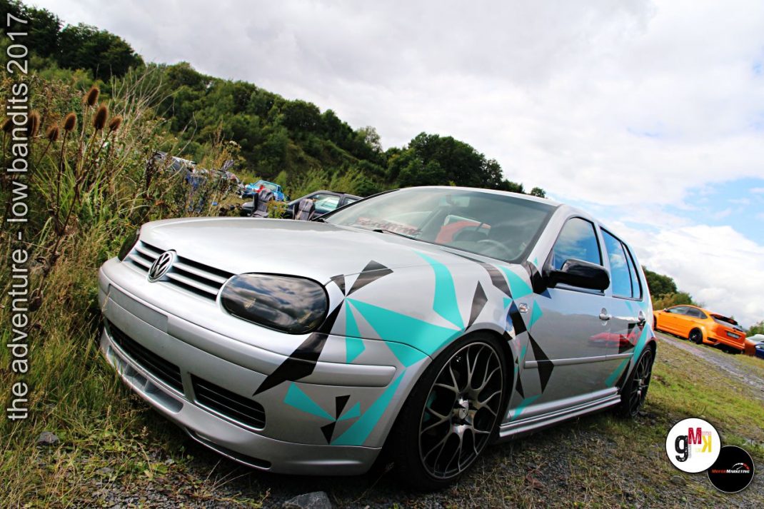 Weiß-türkis gestalteter VW Golf mit Aero-Kit und custom Felgen bei Tuning-Treffen mit weiteren modifizierten Fahrzeugen