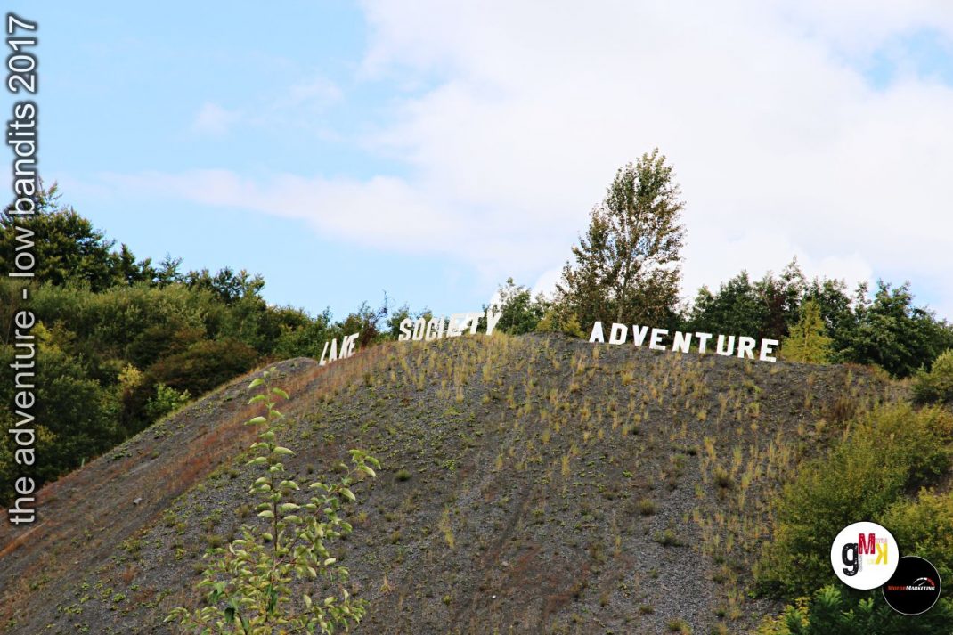 Steinbruch mit weißen Leuchtbuchstaben „the adventure – social adventure" auf bewachsenem Hang, Veranstaltungskulisse 2017