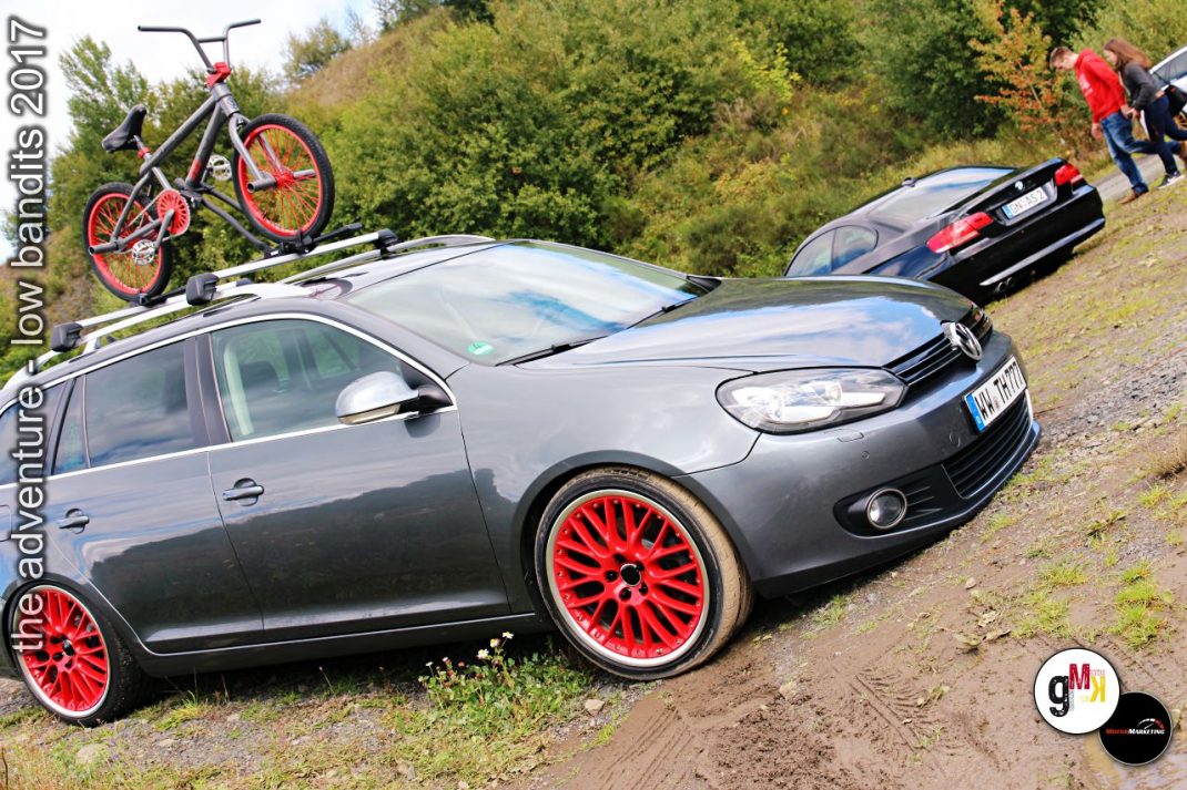 Tiefergelegte Youngtimer mit auffälligen roten Felgen stehen in einem Steinbruch, ein rotes Fixie-Bike auf dem Dach, Teilnehmer einer Tuning-Veranstaltung