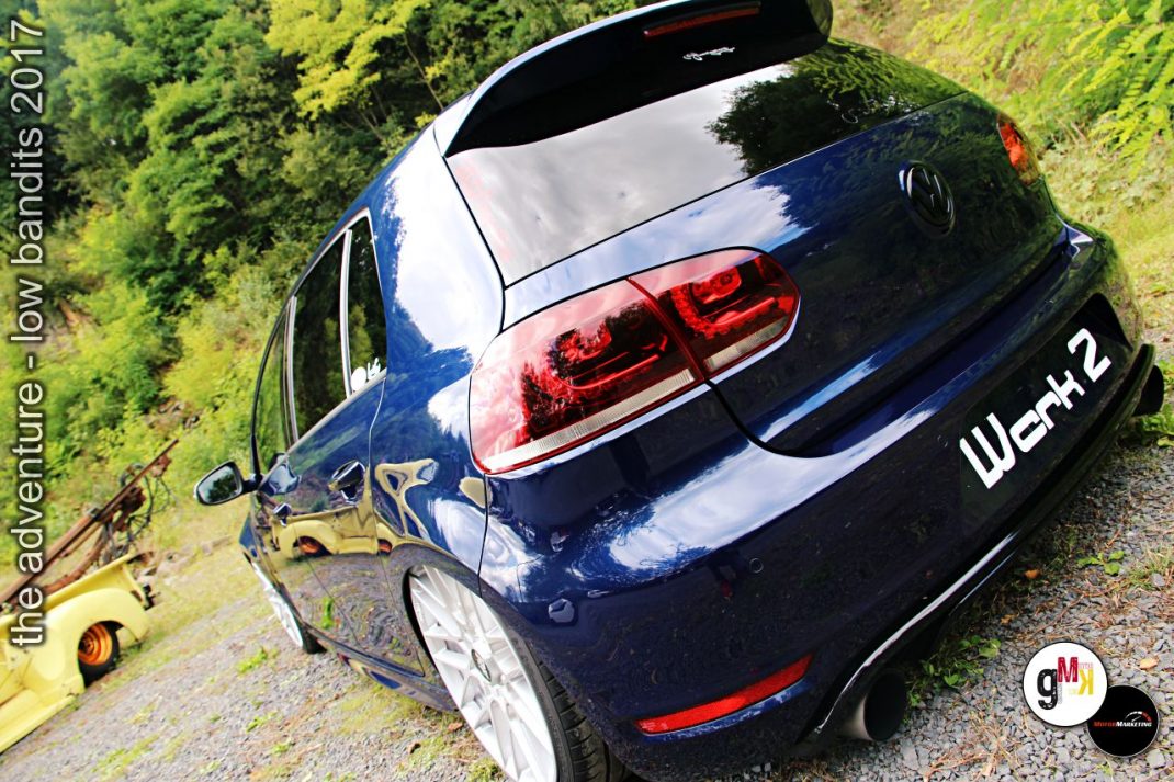 Dunkelblauer VW Golf mit Tuning-Elementen auf Schotterweg neben gelbem Bagger beim Low Bandits Event