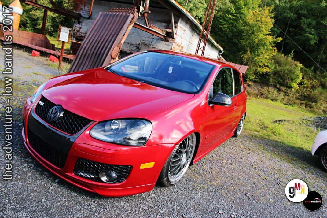 Roter Youngtimer-Sportwagen mit tiefer Lackierung auf Kiesplatz vor Holzschuppen, Tuning-Event in Steinbruchgelände