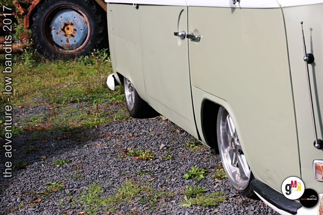Weiße Oldtimer-Lieferwagen auf Kiesplatz neben verrostetem Traktorrad bei der Adventure-low-bandits-Veranstaltung