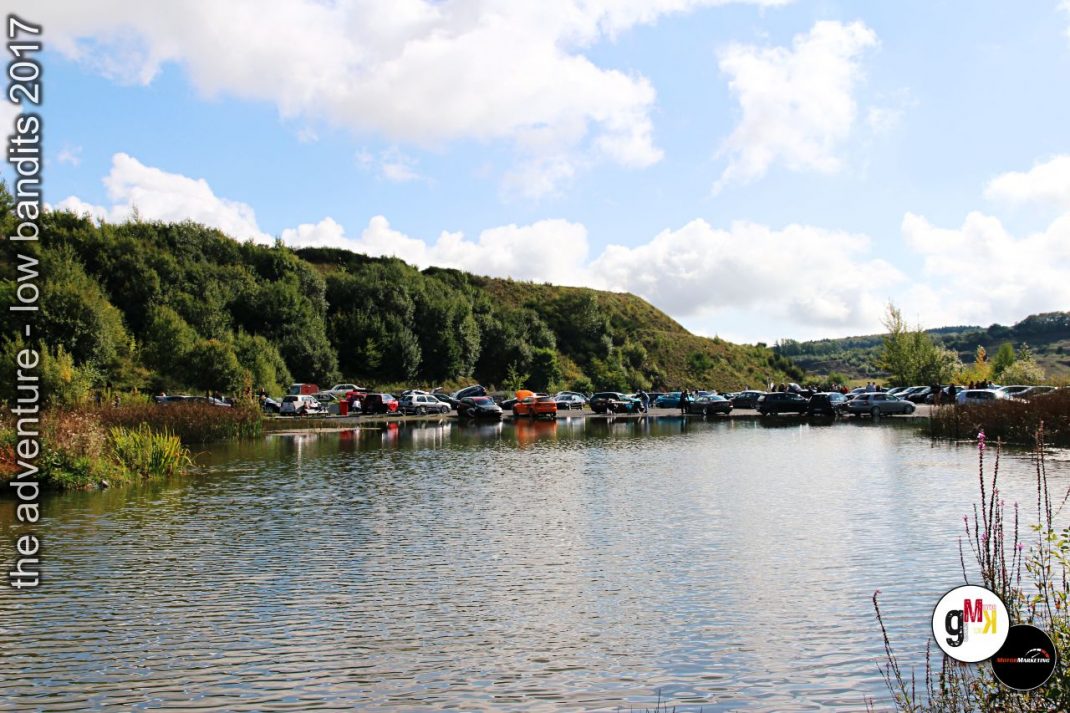 Oldtimer und Youngtimer parken in einer Reihe an einem Fluss unter grünen Hügeln bei der Low Bandits Rallye 2017