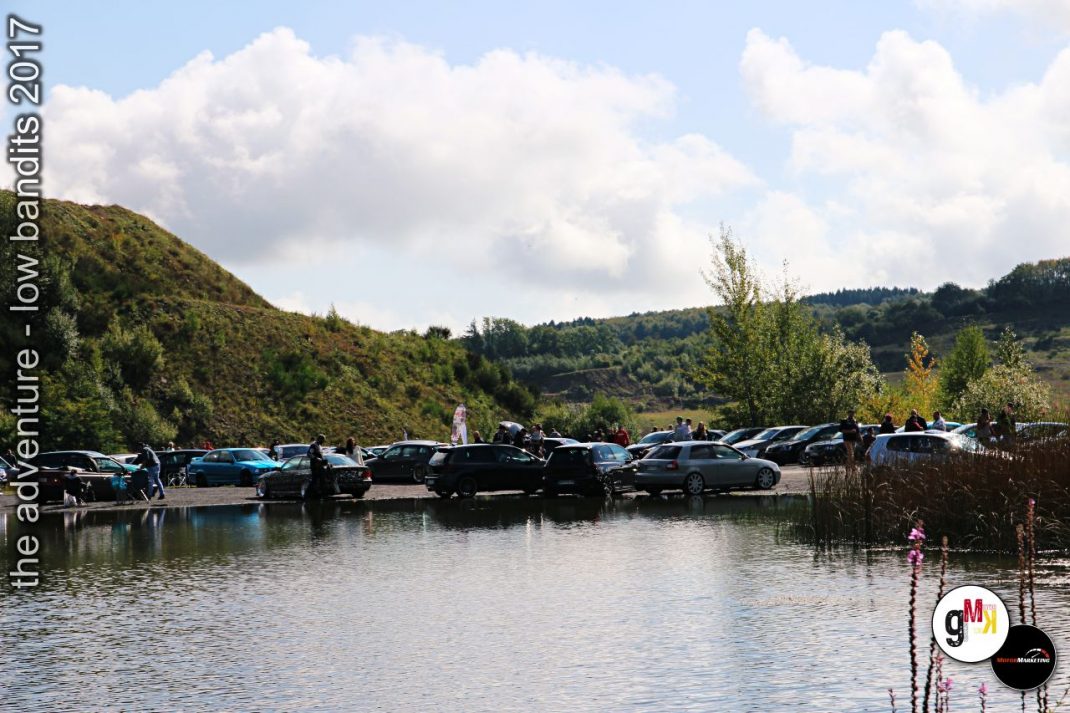 Mehrere Oldtimer und Youngtimer parken an einem See vor bewaldeten Hügeln bei der Low-Bandits-Tour 2017