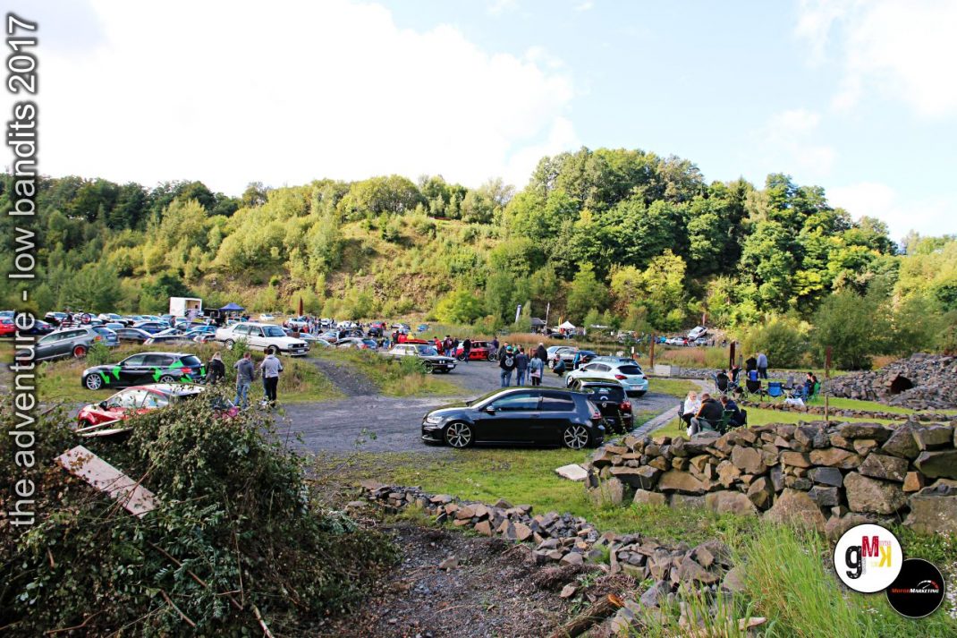 Steinbruch-Gelände mit Oldtimer und Youngtimer auf Treffen, Zuschauer zwischen Fahrzeugen und Trockenmauer, bewaldete Hügellandschaft