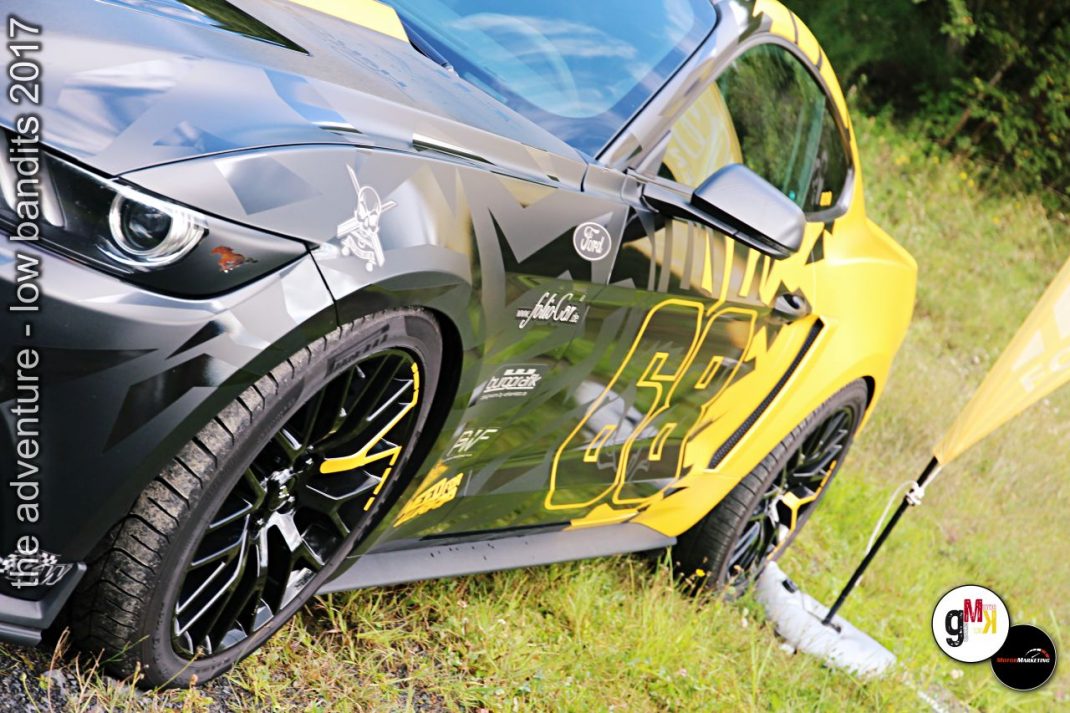 Zwei Youngtimer-Sportwagen mit Tuning-Felgen parken nebeneinander auf Wiese, schwarzer und gelber Wagen mit Spoilern und Custom-Designs bei Low Bandits 2017